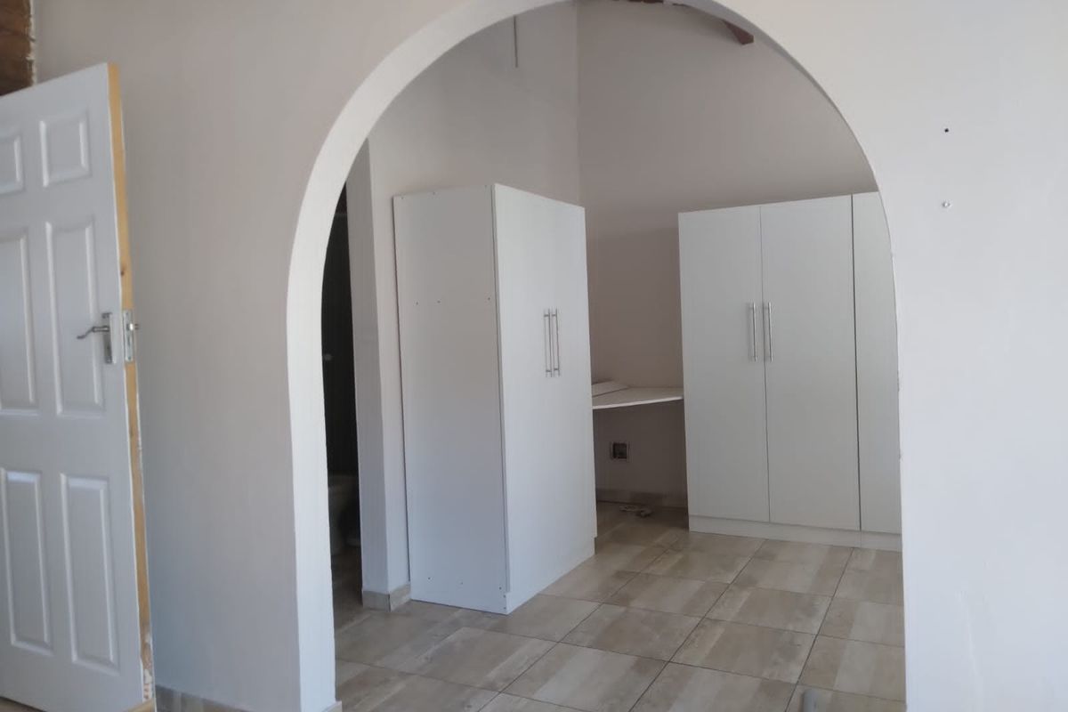 A bedroom interior featuring tiled flooring, an arched entryway, and built-in white cabinetry.