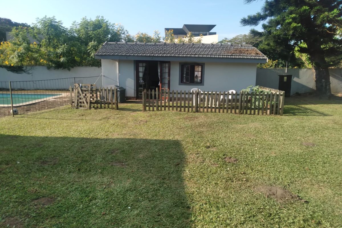 A detached garden outbuilding featuring a tiled roof, set within a spacious backyard with a swimming pool and perimeter fencing.