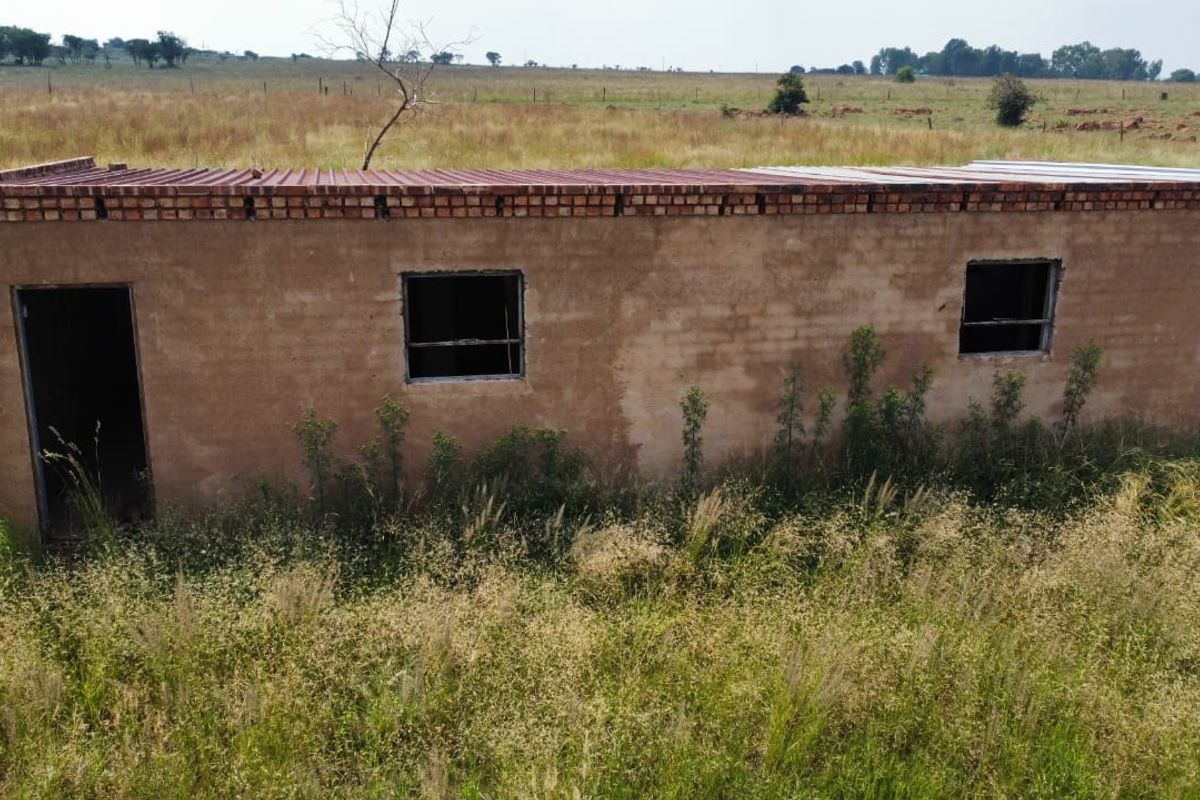 An exterior view of a basic, unplastered masonry farm structure with a corrugated metal roof, currently in a state of disrepair.