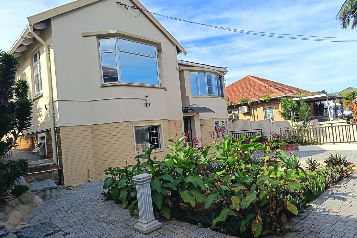 A well-maintained double-story residential property featuring a paved courtyard, landscaped garden beds, and large bay windows.