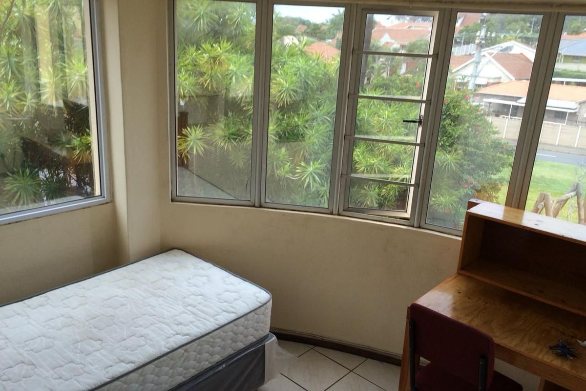 A bedroom featuring large windows with neighbourhood views, tiled flooring, and ample natural light.