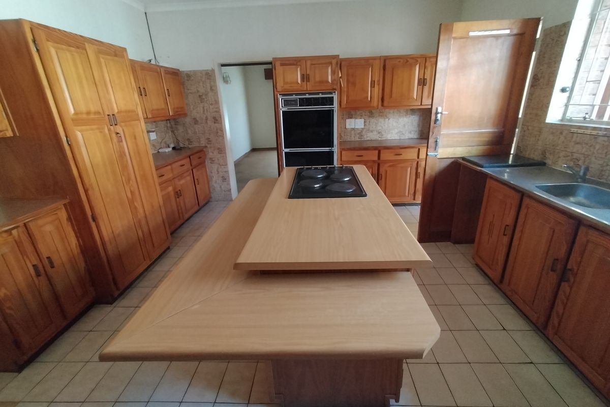 Spacious kitchen featuring extensive wooden cabinetry, a central island with an integrated hob, built-in oven, and tiled flooring.
