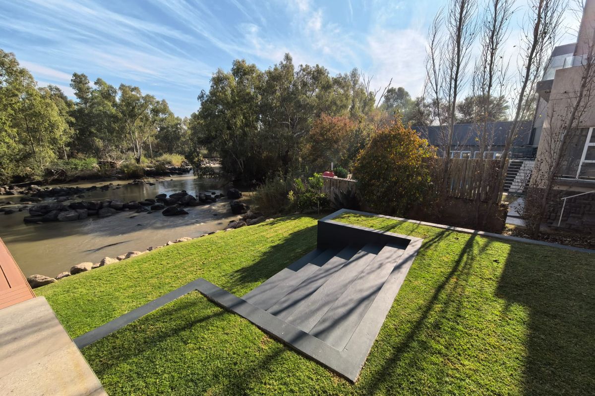 A well-maintained rear garden featuring a modern sunken deck area with direct views overlooking the adjacent river.