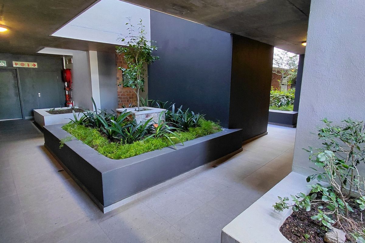 A modern, well-maintained outdoor courtyard area featuring built-in concrete planters, tiled flooring, and architectural recessed lighting.