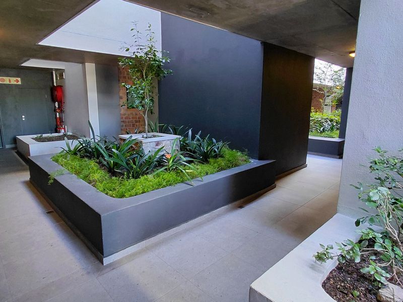 A modern, well-maintained outdoor courtyard area featuring built-in concrete planters, tiled flooring, and architectural recessed lighting.
