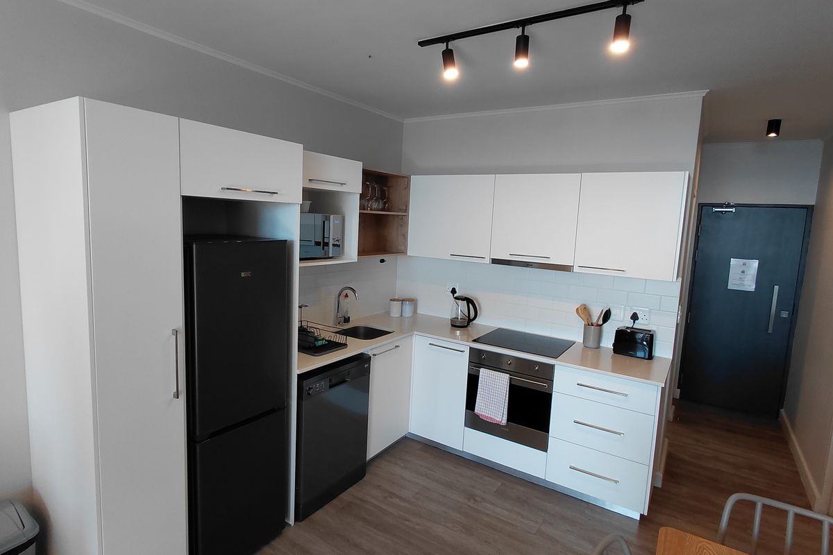 Modern kitchen featuring white cabinetry, subway tile backsplash, integrated appliances, electric hob, oven, and contemporary track lighting in an open-plan layout.