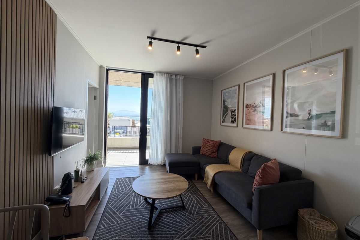Modern living room featuring stylish slatted timber wall paneling, track lighting, and direct access to a balcony with scenic views.