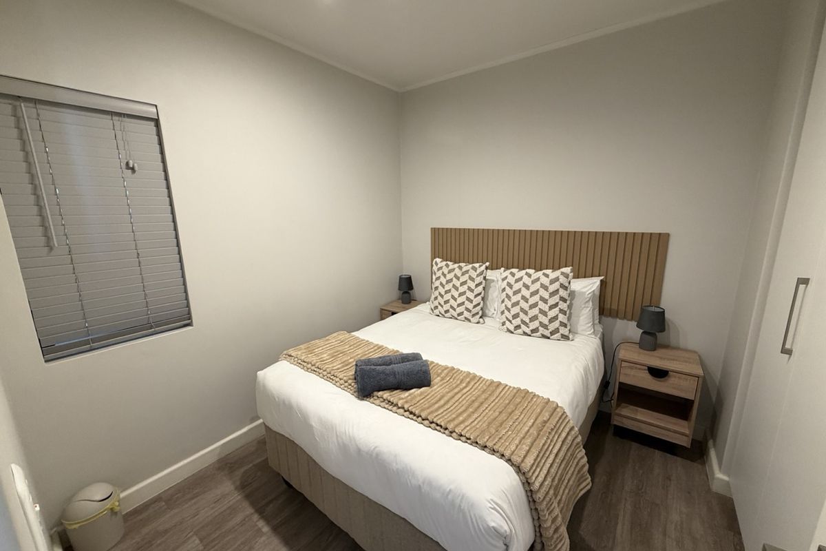 A well-maintained bedroom featuring laminate flooring, a modern slatted headboard, and a built-in wardrobe with neutral wall finishes.