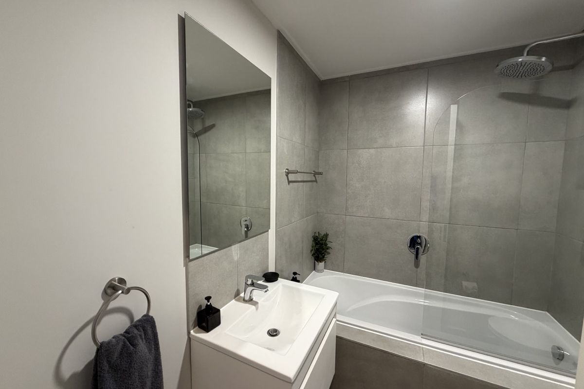 Modern bathroom featuring a sleek vanity, wall-mounted mirror, and a combined bathtub and shower with contemporary grey tiling and glass screen.