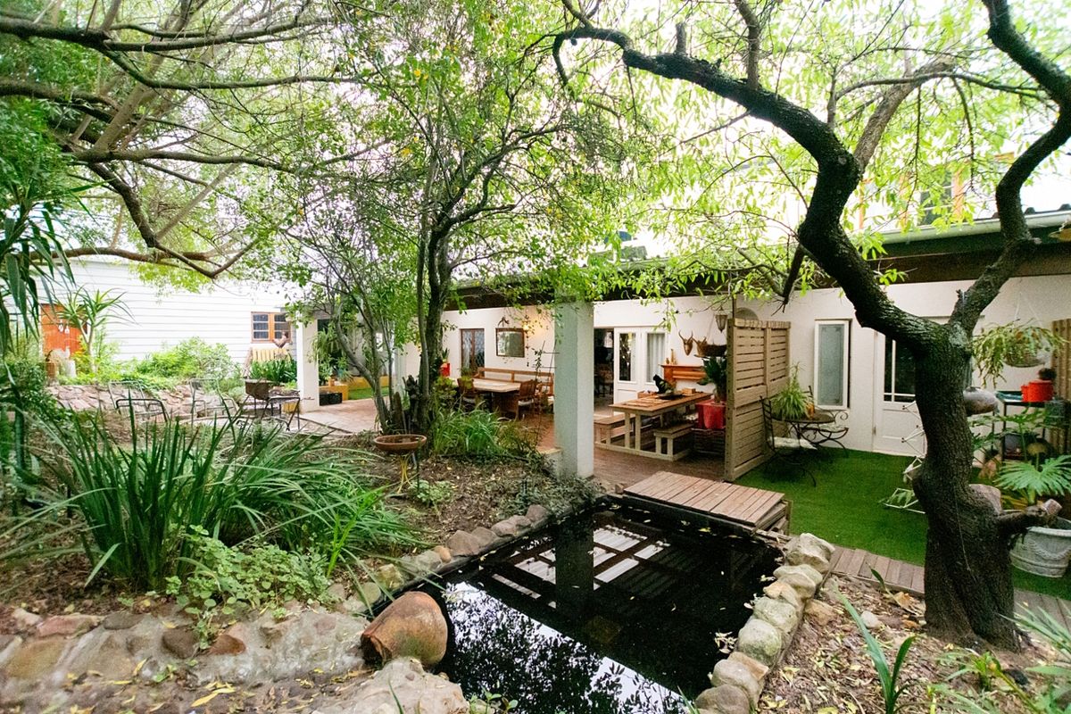A rear garden area featuring a small pond, mature trees, and a covered patio space providing an outdoor entertainment area.