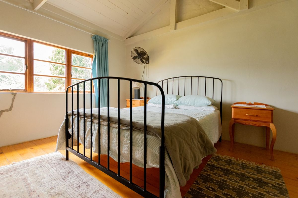 A bedroom featuring exposed timber ceiling beams, polished wooden flooring, and large windows providing natural light.