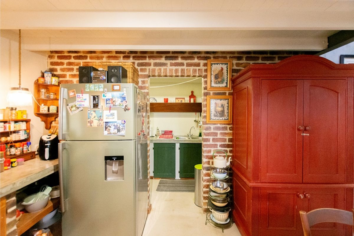 A rustic kitchen area featuring exposed brick walls, built-in cabinetry, and a functional scullery space visible through the arched doorway.