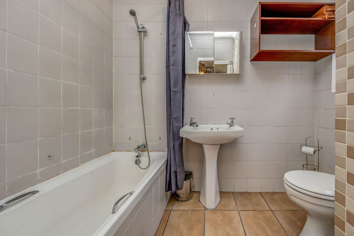 A functional bathroom featuring a bathtub with shower attachment, pedestal sink, and toilet, finished with neutral wall and floor tiling.