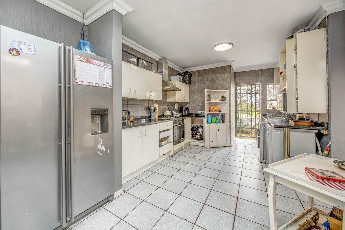 A functional kitchen featuring tiled flooring, built-in cabinetry, and a tiled splashback, offering a practical layout with direct access to the exterior.