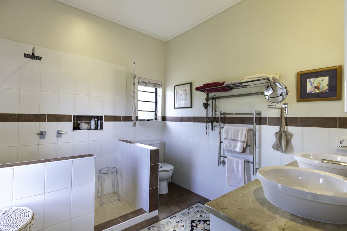 A functional bathroom featuring a walk-in shower with a recessed niche, dual vanity with stone countertop, and a heated towel rail.