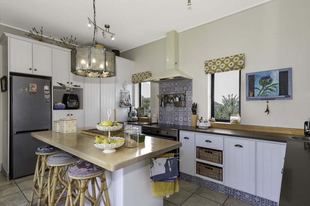 A well-maintained kitchen featuring white cabinetry, a wooden island countertop, integrated oven, extractor fan, and decorative tiled splashback with ample natural light.