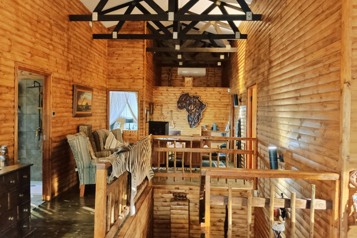 A rustic living area featuring extensive timber wall cladding, exposed vaulted ceiling trusses, and a wooden staircase with a matching balustrade.