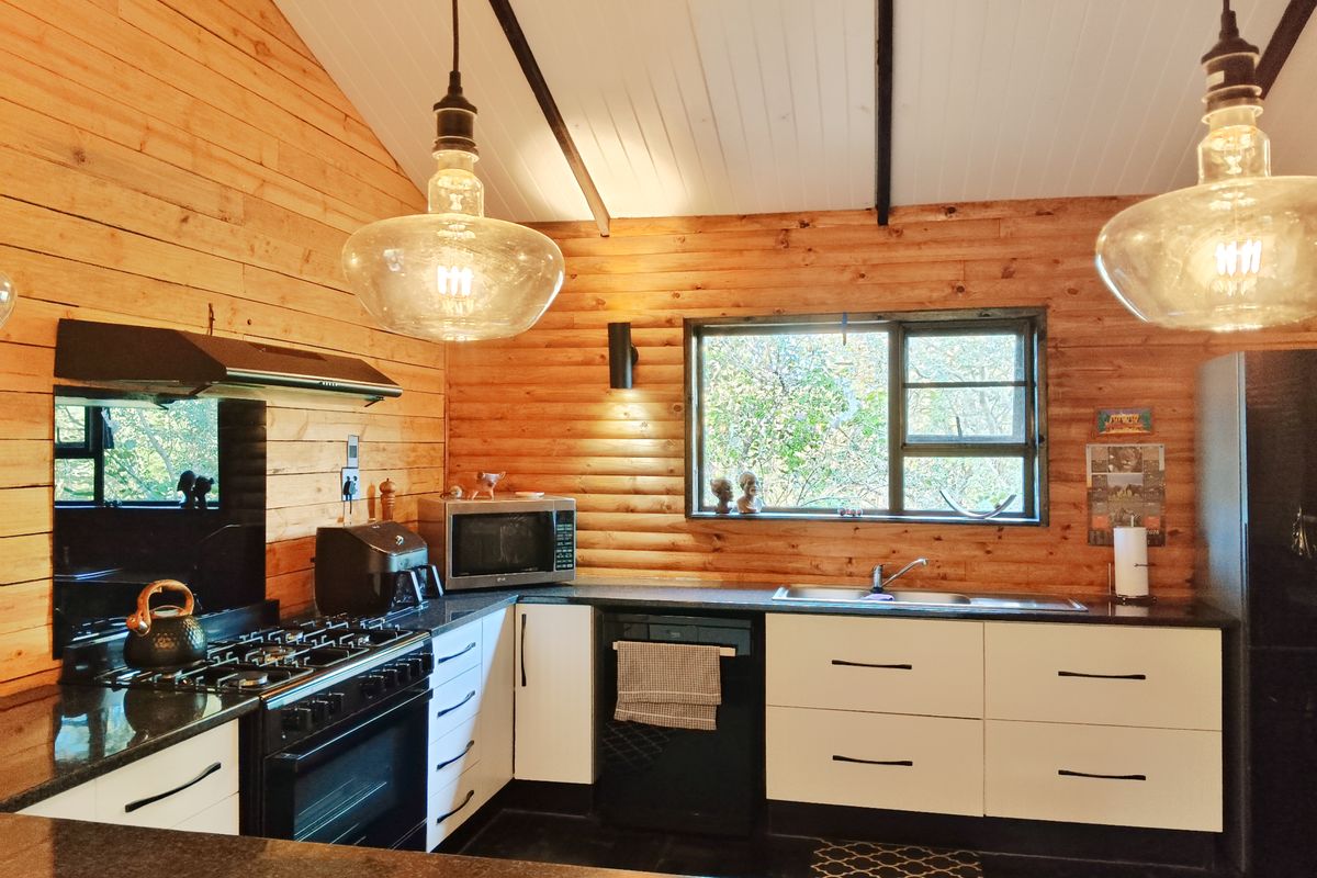 A rustic-style kitchen featuring timber wall cladding, exposed beams, granite countertops, a gas stove with extractor, and modern white cabinetry.