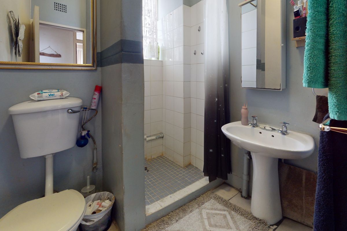 A functional bathroom featuring a pedestal basin, toilet, and a tiled shower enclosure with a curtain, offering potential for modernization and cosmetic updates.