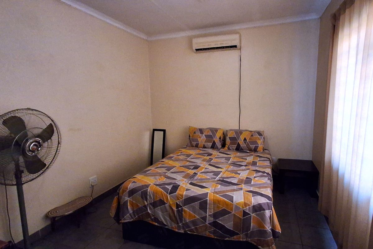 A functional bedroom featuring tiled flooring, a wall-mounted split-system air conditioner, and vertical window blinds.