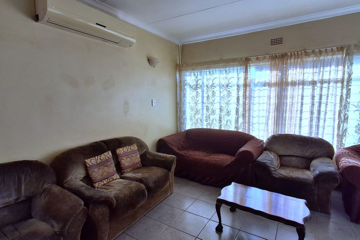 A living room featuring tiled flooring, a wall-mounted air conditioning unit, and large windows, currently showing signs of wear on the wall surfaces.