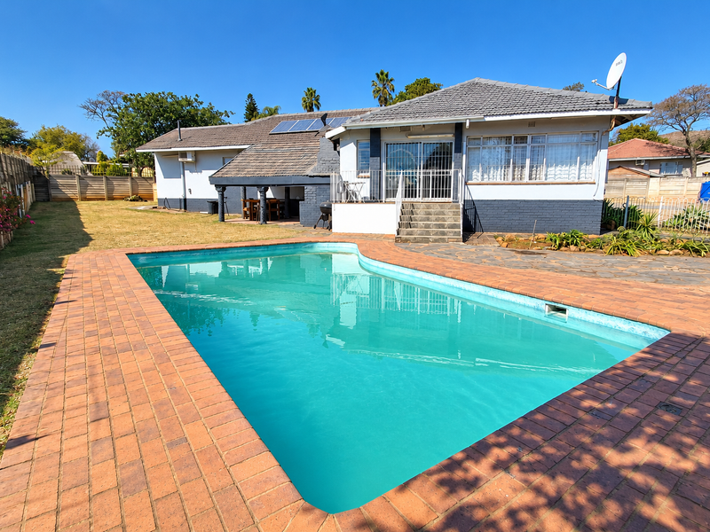 Rear exterior view featuring a swimming pool with brick paving, a covered patio area, and solar panels installed on the tiled roof.