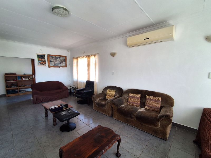 A spacious living room featuring tiled flooring, a wall-mounted split-system air conditioner, and neutral wall finishes, offering a functional layout for relaxation.