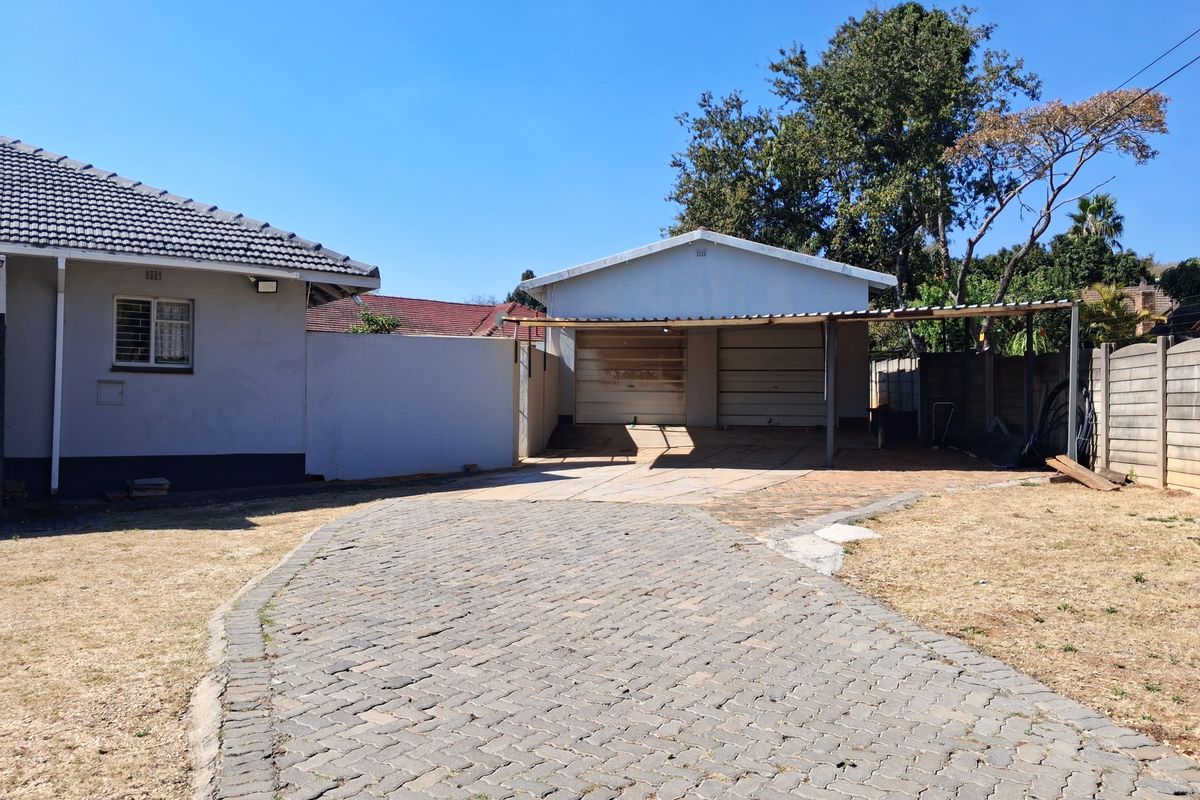 Rear exterior view featuring a paved driveway, double garage with an attached carport, and perimeter boundary walls.