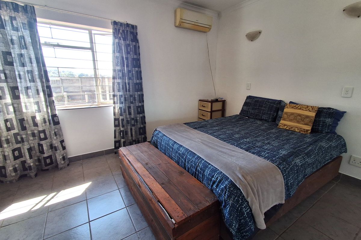 A functional bedroom featuring tiled flooring, a wall-mounted air conditioning unit, and security bars on the window.