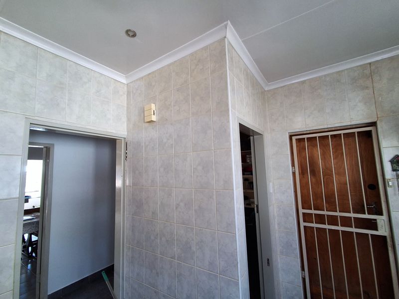 A functional hallway area featuring tiled walls, recessed downlighting, and a secure metal gate, providing access to adjacent rooms.