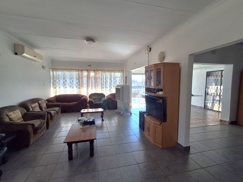 Spacious living room featuring neutral tiled flooring and a wall-mounted air conditioning unit, offering a functional layout with access to adjacent areas.