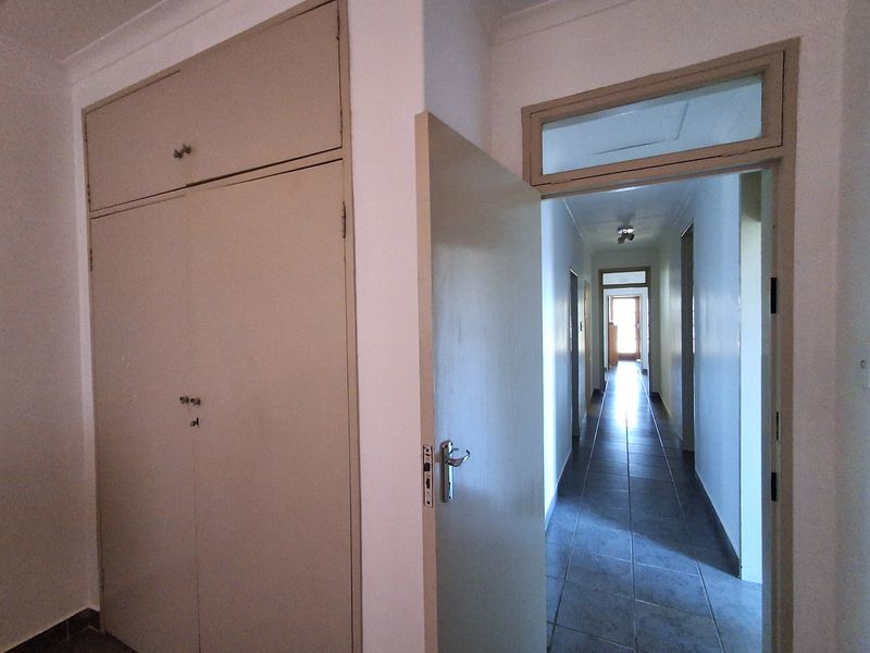A functional hallway featuring tiled flooring, built-in storage cupboards, and a transom window above the doorway, providing access to other areas of the home.