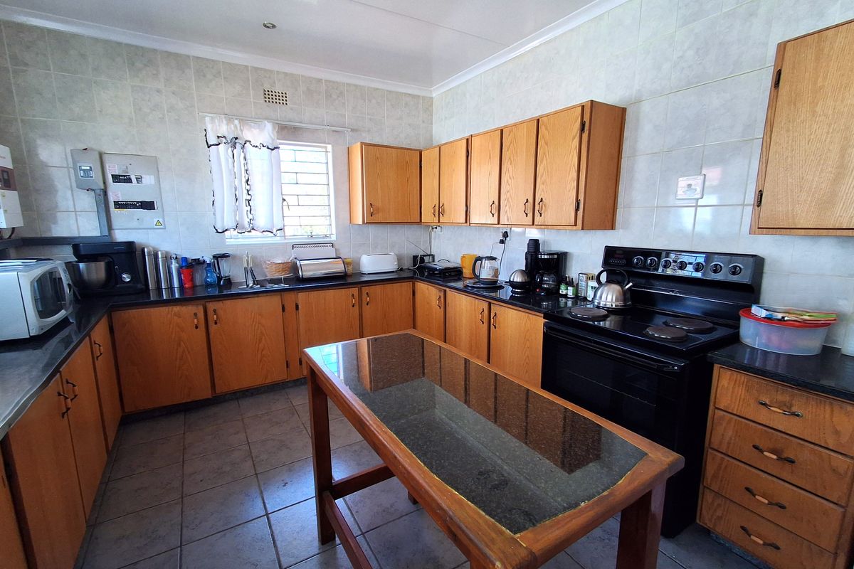 A functional kitchen featuring wooden cabinetry, tiled splashbacks, tiled flooring, and a freestanding electric stove with a central prep island.