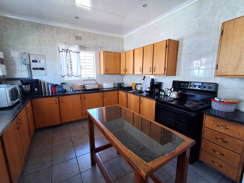 A functional kitchen featuring wooden cabinetry, tiled splashbacks, tiled flooring, and a freestanding electric stove with a central prep island.