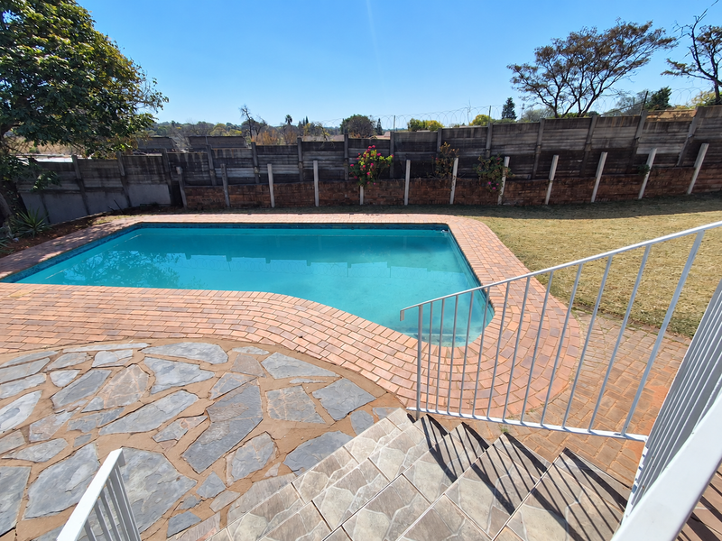 Outdoor pool area featuring a swimming pool with brick coping, stone paved patio, and metal balustrade, set against a perimeter boundary wall.