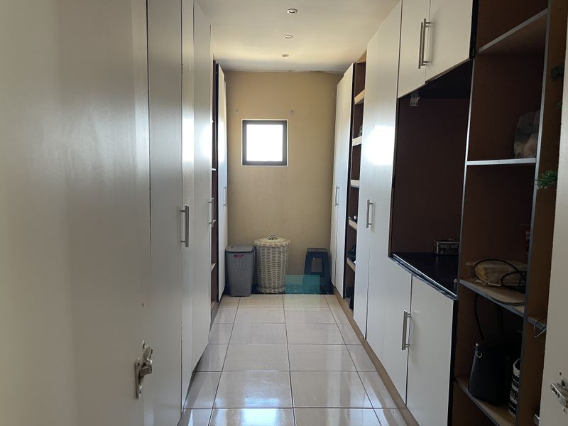 A functional utility space or walk-in storage area featuring extensive built-in cabinetry, tiled flooring, and recessed lighting.