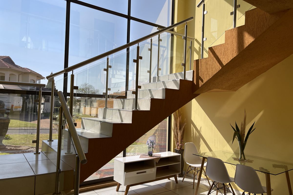Bright entrance area featuring a modern staircase with glass balustrades, stainless steel handrails, and expansive floor-to-ceiling windows providing ample natural light.