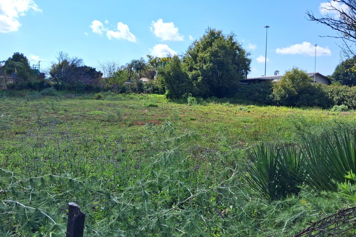 A view of a vacant residential plot featuring natural vegetation, mature trees, and perimeter wire fencing.