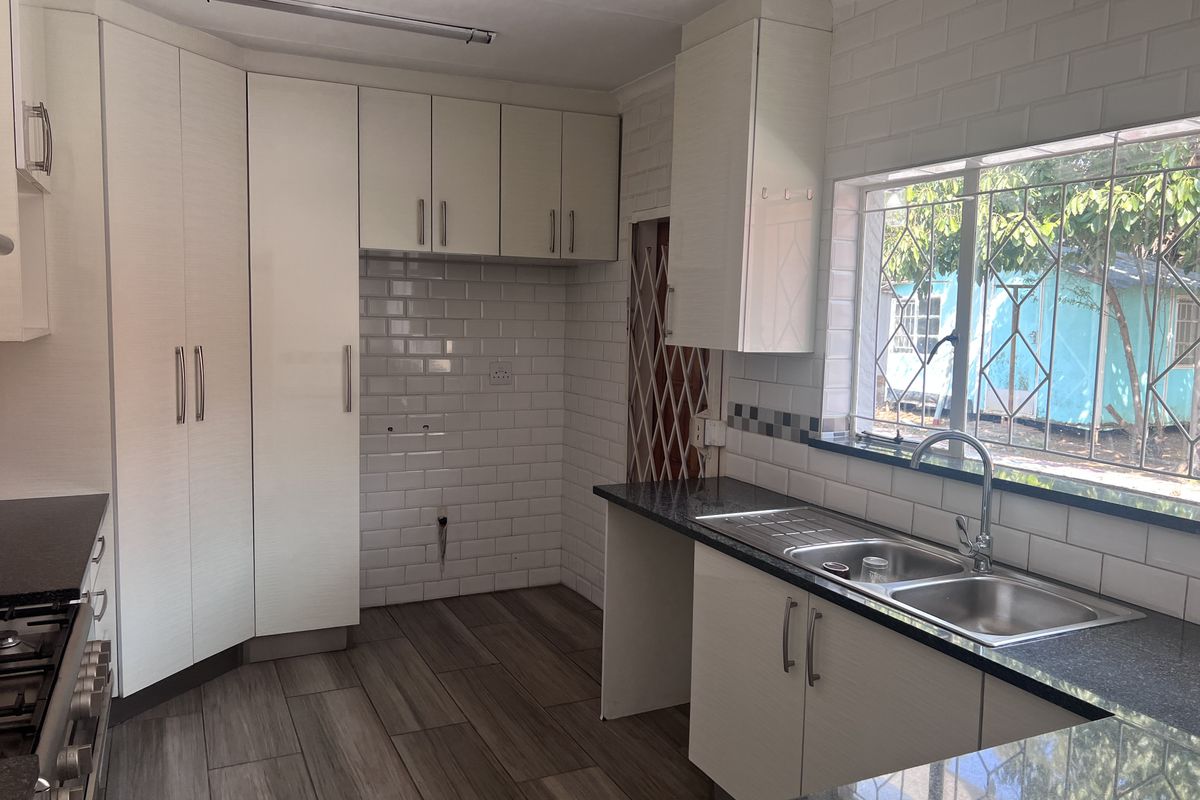 A clean, modern kitchen featuring white cabinetry, subway tile backsplash, granite countertops, and a double bowl stainless steel sink with a gooseneck faucet.