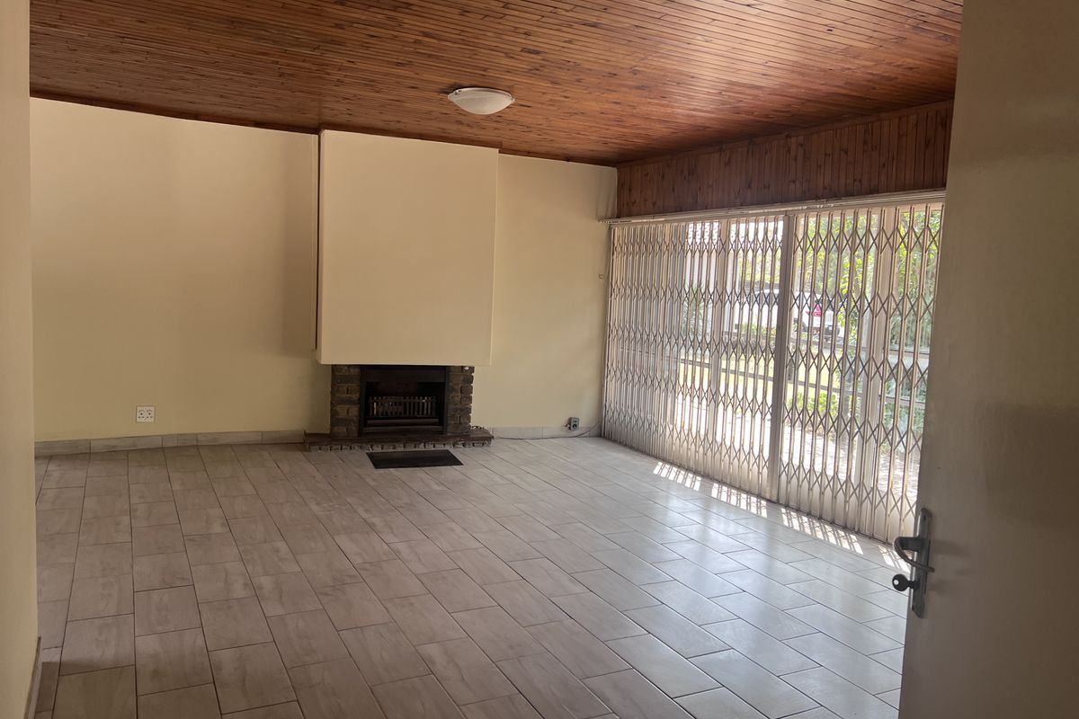 Spacious living room featuring a timber ceiling, tiled flooring, and a built-in brick fireplace, with large sliding doors leading to the exterior.