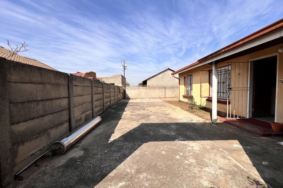 A rear exterior view of the property featuring a concrete driveway and a precast concrete boundary wall.