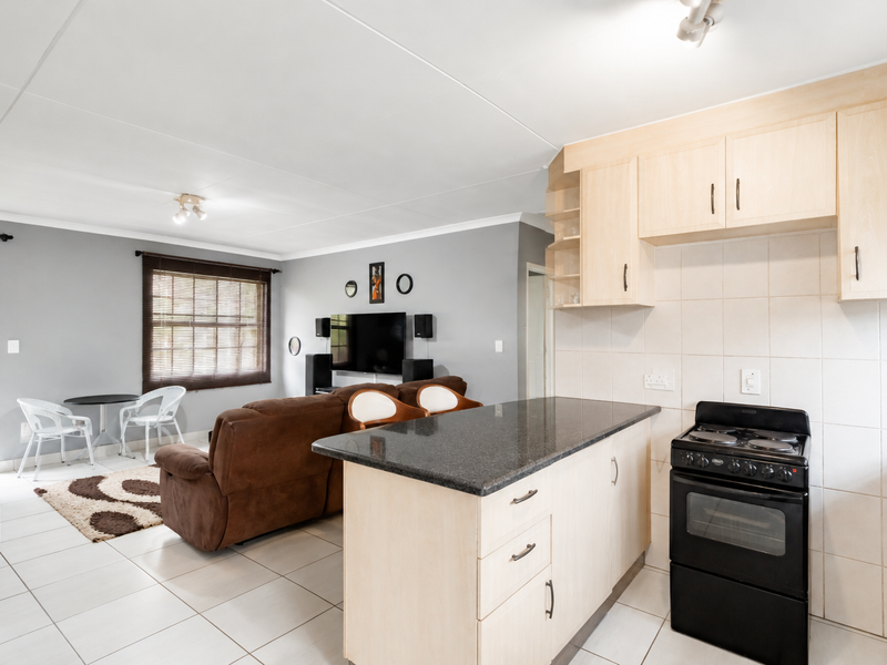 Open-plan living area featuring a functional kitchen with granite countertops, built-in cabinetry, and a tiled floor, seamlessly flowing into the adjacent lounge space.