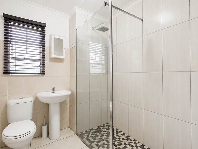 A clean, modern bathroom featuring a pedestal basin, a walk-in shower with a glass screen, and neutral wall tiling.