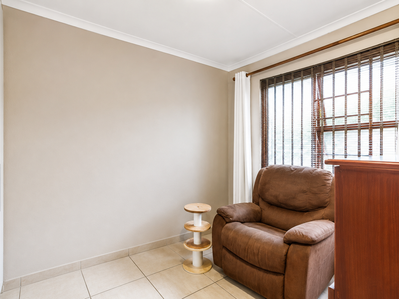 A well-maintained bedroom featuring neutral wall tones, tiled flooring, and a built-in wardrobe, complemented by natural light through venetian blinds.