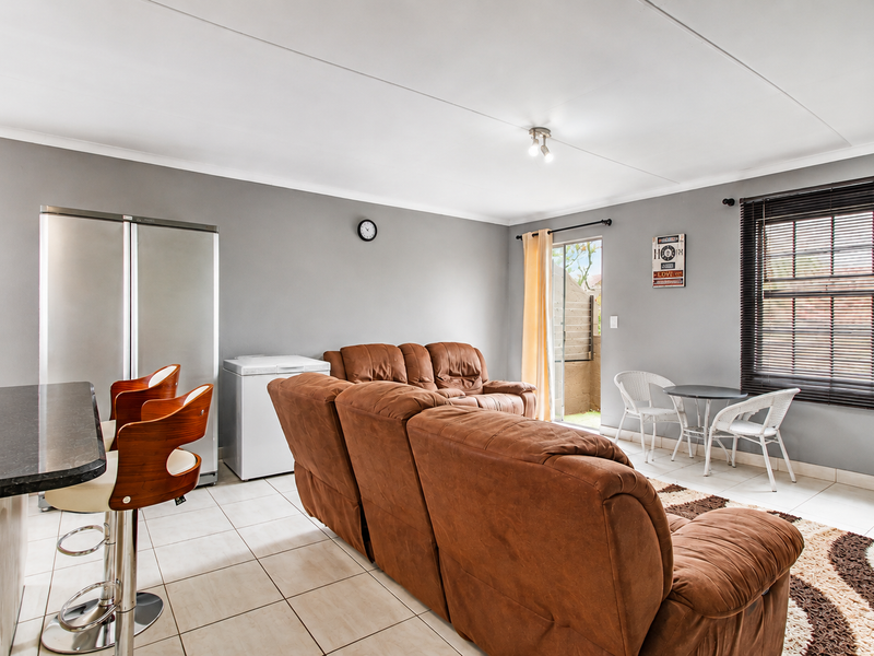 Open plan living area featuring tiled flooring, a breakfast bar, and direct access to an outdoor patio through a sliding door.