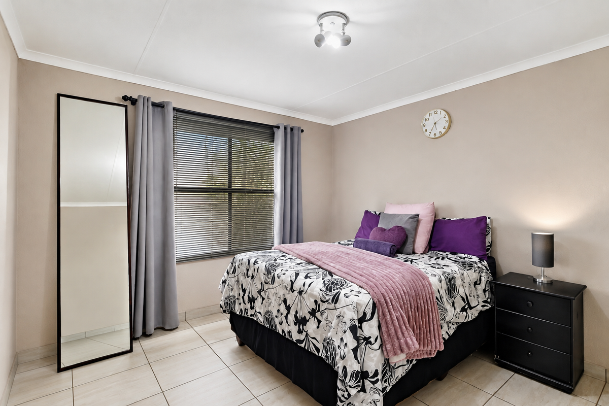 A well-maintained bedroom featuring neutral wall tones, tiled flooring, and a window fitted with venetian blinds and curtains.