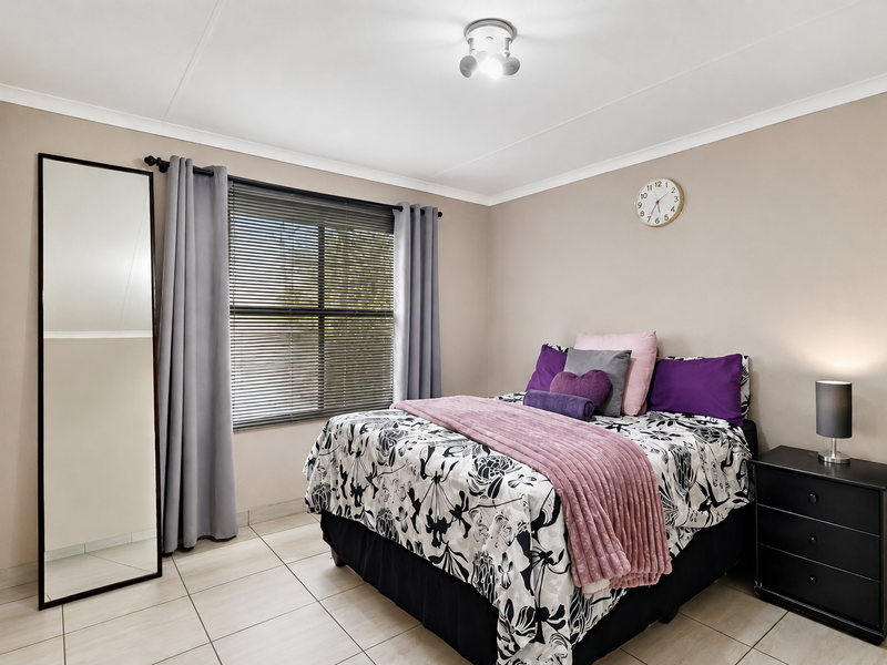A well-maintained bedroom featuring neutral wall tones, tiled flooring, and a window fitted with venetian blinds and curtains.