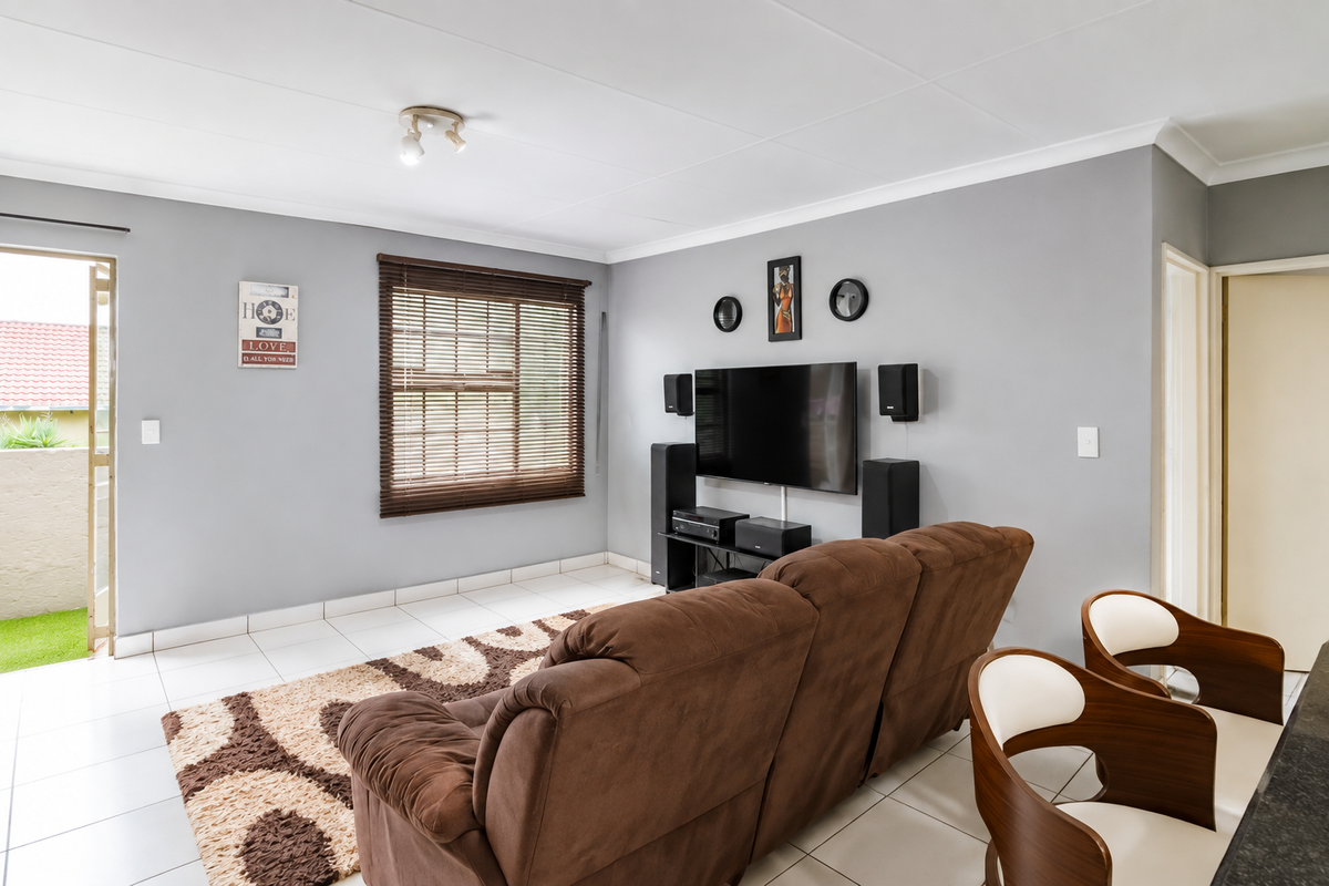 A well-lit living room featuring tiled flooring, coved ceilings, and a window with venetian blinds, providing direct access to an outdoor patio area.