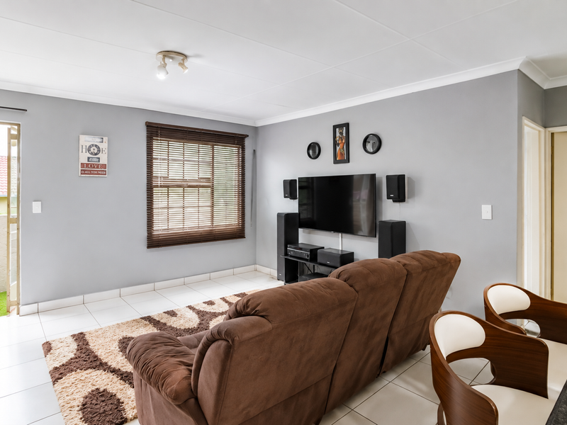 A well-lit living room featuring tiled flooring, coved ceilings, and a window with venetian blinds, providing direct access to an outdoor patio area.