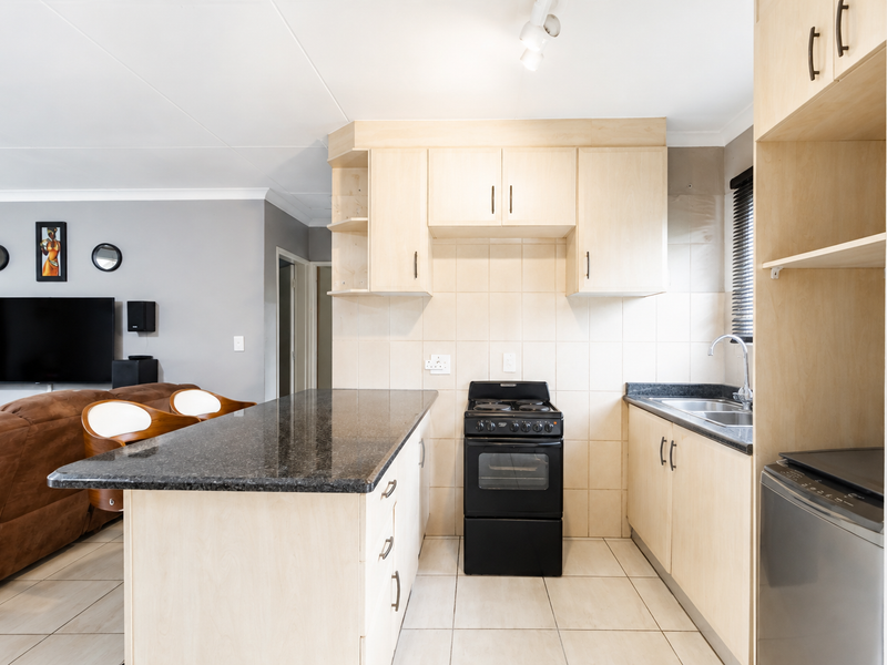 Open-plan kitchen featuring light wood cabinetry, granite countertops, a tiled backsplash, and a freestanding stove, seamlessly flowing into the adjacent living area.